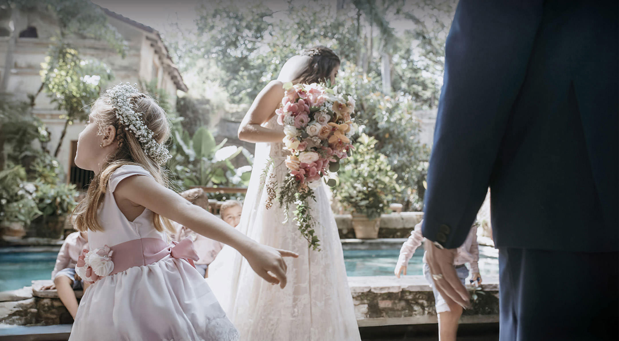 Breathless Weddings Bride holding bouquet near a pool while a flower girl plays around.